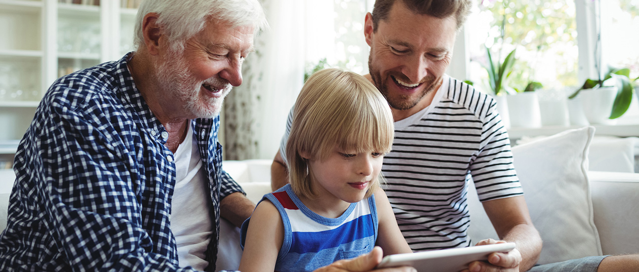 Boy using digital tablet with his father and grandfather in living room-hero